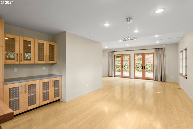 unfurnished living room with an inviting chandelier, french doors, and light wood-type flooring