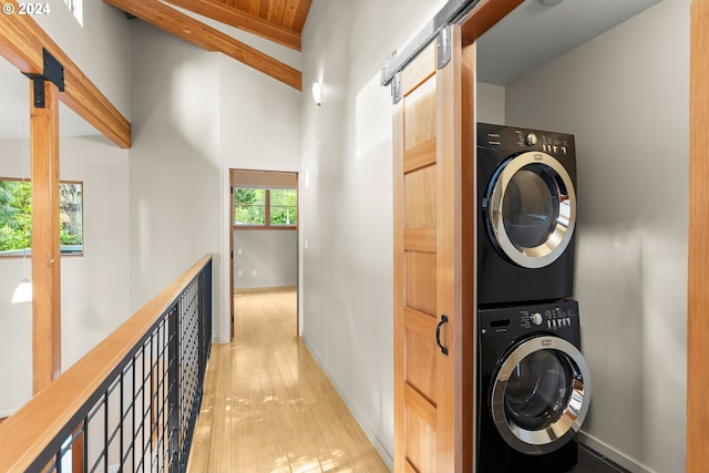 laundry area featuring wood ceiling, a barn door, stacked washer and dryer, and light wood-type flooring