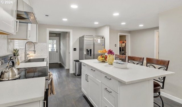 kitchen featuring white cabinetry, appliances with stainless steel finishes, a kitchen bar, dark wood-type flooring, and a center island