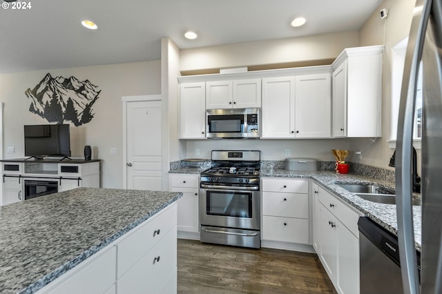 kitchen with stainless steel appliances, sink, light stone countertops, white cabinetry, and dark hardwood / wood-style flooring