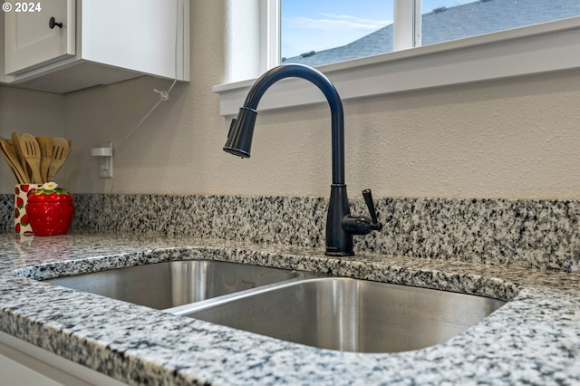 interior details with sink, white cabinetry, and stone countertops