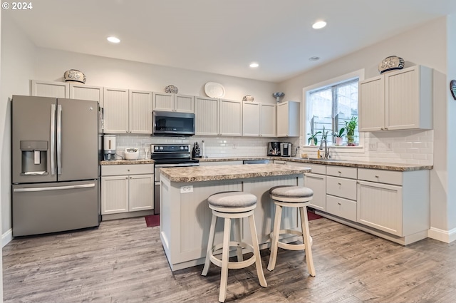 kitchen with a center island, white cabinetry, appliances with stainless steel finishes, a kitchen breakfast bar, and light hardwood / wood-style flooring