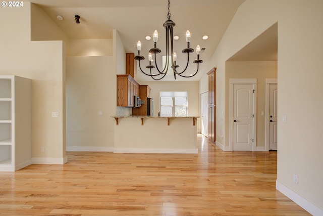 kitchen with kitchen peninsula, a kitchen breakfast bar, light wood-type flooring, light stone counters, and a notable chandelier