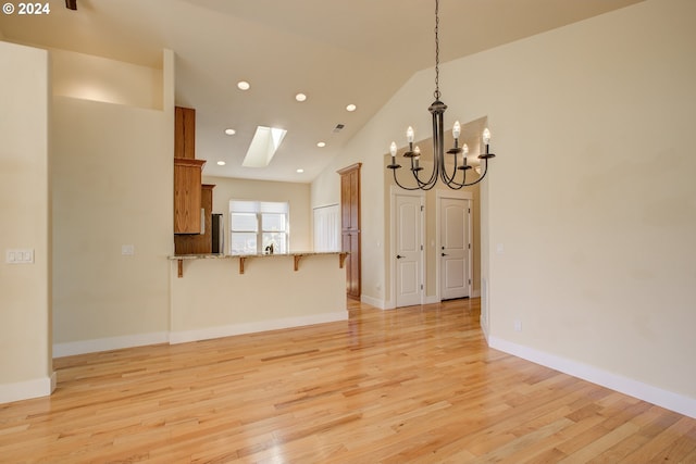 unfurnished living room featuring a skylight, light hardwood / wood-style flooring, high vaulted ceiling, and a notable chandelier