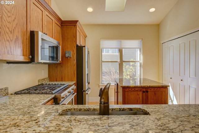 kitchen featuring kitchen peninsula, light stone countertops, sink, and stainless steel appliances