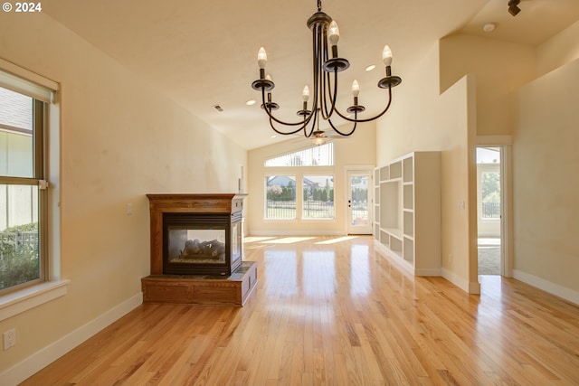 unfurnished living room with a chandelier, a healthy amount of sunlight, lofted ceiling, and light hardwood / wood-style flooring