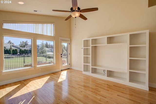 unfurnished living room with ceiling fan, a towering ceiling, and light hardwood / wood-style flooring