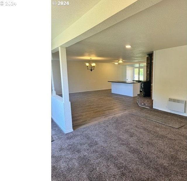 unfurnished living room featuring a wood stove, dark wood-type flooring, a textured ceiling, and a notable chandelier