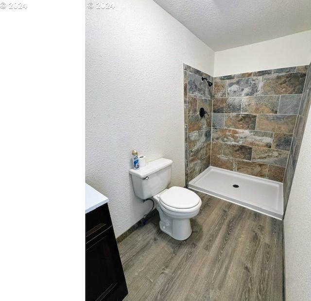 bathroom featuring a tile shower, vanity, a textured ceiling, wood-type flooring, and toilet