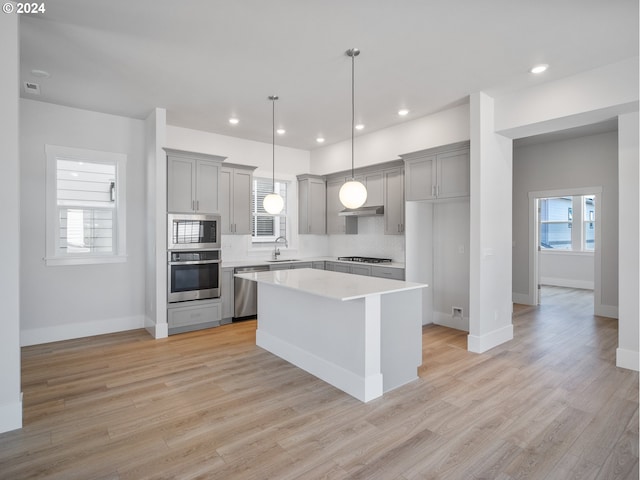 kitchen with sink, stainless steel appliances, a center island, decorative backsplash, and light wood-type flooring