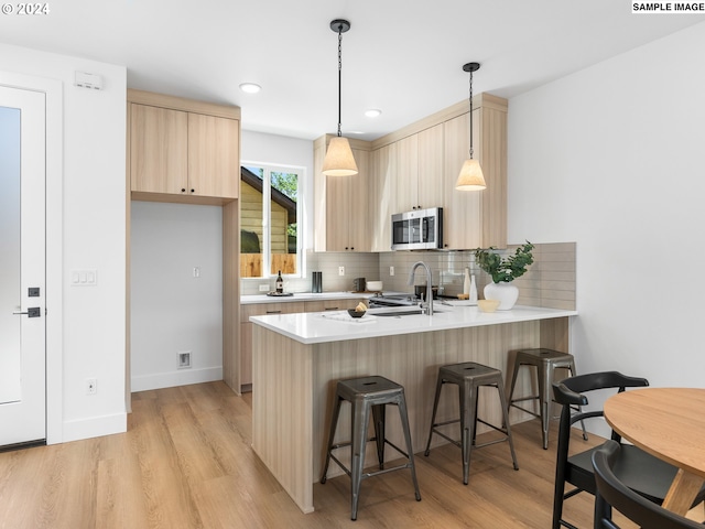 kitchen featuring sink, light hardwood / wood-style flooring, light brown cabinetry, decorative light fixtures, and kitchen peninsula