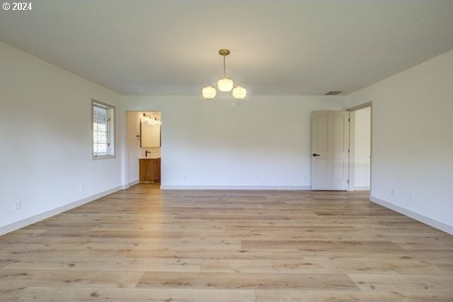 spare room featuring a chandelier and light hardwood / wood-style flooring