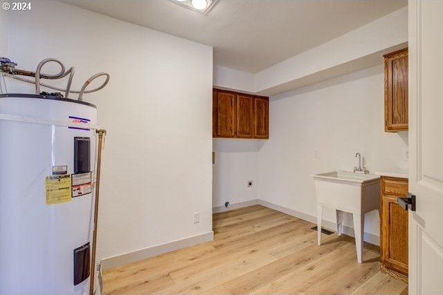 laundry area featuring water heater, cabinets, hookup for an electric dryer, and light hardwood / wood-style flooring