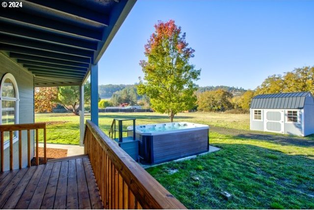 wooden deck featuring a lawn, a hot tub, and a storage shed