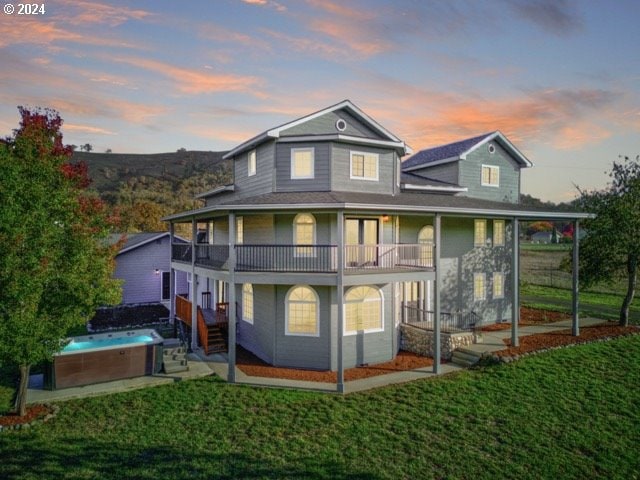 back house at dusk featuring a balcony, a hot tub, and a yard