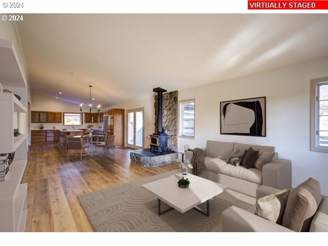 living room featuring lofted ceiling, a notable chandelier, light hardwood / wood-style floors, and a wood stove