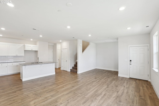 kitchen with sink, white cabinetry, tasteful backsplash, light hardwood / wood-style floors, and a center island with sink