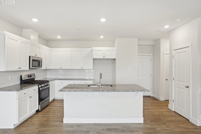 kitchen with stainless steel appliances, an island with sink, white cabinetry, dark stone countertops, and sink