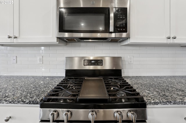 kitchen with appliances with stainless steel finishes, white cabinetry, dark stone counters, and backsplash