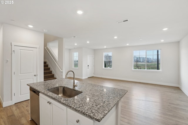 kitchen with an island with sink, light stone countertops, sink, white cabinetry, and stainless steel dishwasher