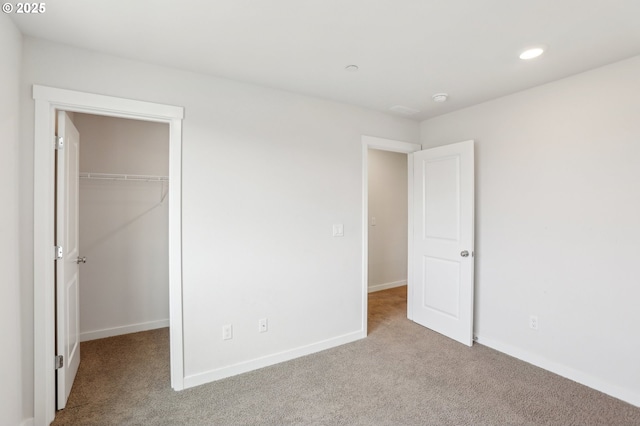 unfurnished bedroom with a walk in closet, a closet, and light carpet