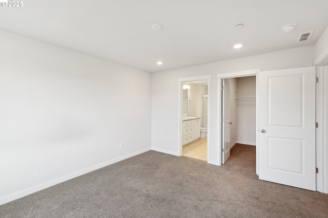 unfurnished bedroom featuring a spacious closet, ensuite bathroom, a closet, and light carpet