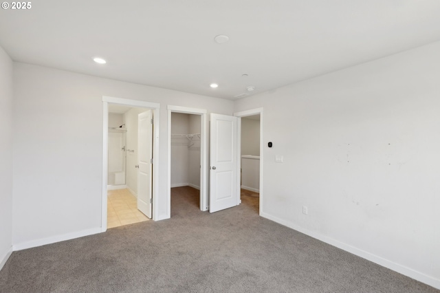 unfurnished bedroom featuring a walk in closet, connected bathroom, a closet, and light carpet