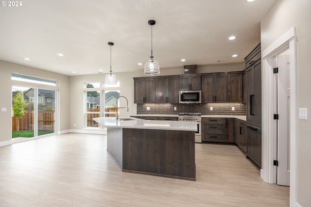 kitchen with decorative backsplash, appliances with stainless steel finishes, dark brown cabinets, pendant lighting, and an island with sink