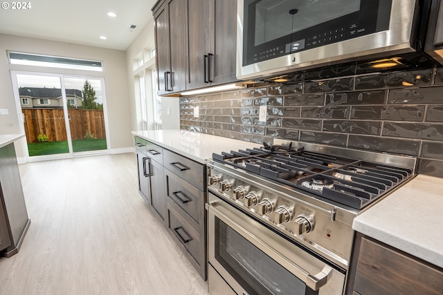 kitchen featuring decorative backsplash, appliances with stainless steel finishes, dark brown cabinetry, and light hardwood / wood-style flooring