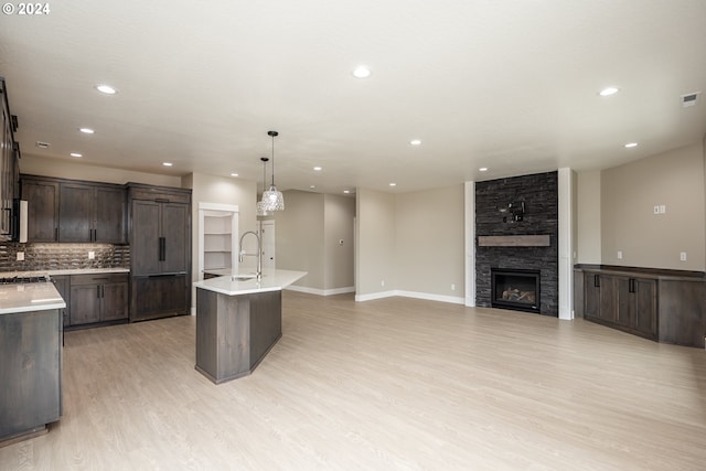 kitchen with sink, decorative light fixtures, dark brown cabinets, a center island with sink, and light wood-type flooring