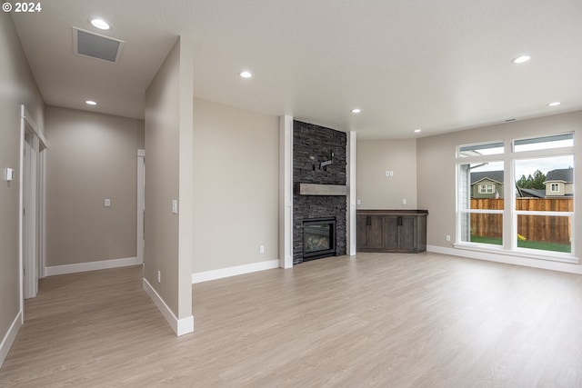 unfurnished living room with a stone fireplace and light hardwood / wood-style floors