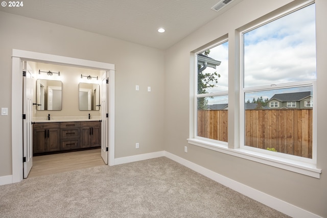 unfurnished bedroom featuring sink, light carpet, and ensuite bath