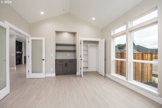 unfurnished bedroom featuring multiple windows, a stone fireplace, light hardwood / wood-style floors, and french doors