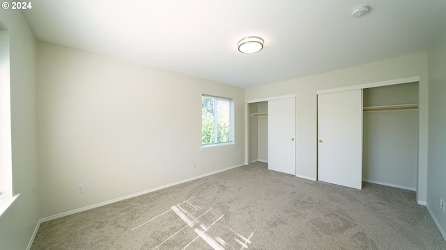 unfurnished bedroom with multiple closets and light colored carpet