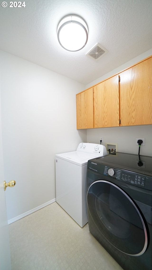 laundry area with a textured ceiling, washing machine and dryer, and cabinets