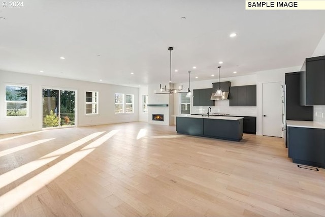 kitchen featuring wall chimney exhaust hood, sink, a kitchen island with sink, pendant lighting, and light hardwood / wood-style floors