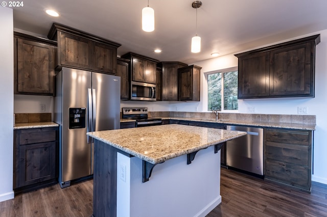 kitchen featuring dark hardwood / wood-style flooring, hanging light fixtures, a center island, light stone counters, and stainless steel appliances