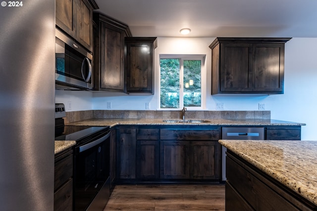 kitchen with sink, appliances with stainless steel finishes, dark brown cabinets, light stone counters, and dark hardwood / wood-style flooring