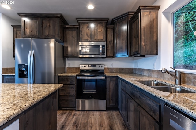 kitchen featuring appliances with stainless steel finishes, sink, dark hardwood / wood-style flooring, light stone countertops, and a healthy amount of sunlight