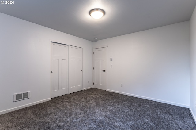 unfurnished bedroom featuring dark carpet and a closet