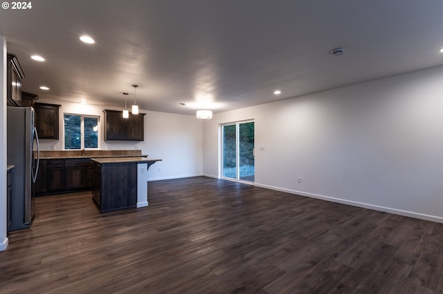 kitchen with dark wood-type flooring, stainless steel refrigerator, a kitchen island, a kitchen bar, and decorative light fixtures