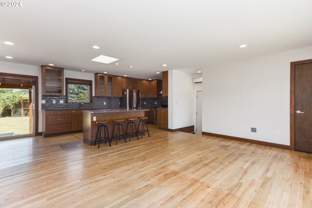 kitchen with decorative backsplash, a kitchen bar, light hardwood / wood-style flooring, stainless steel fridge, and a kitchen island