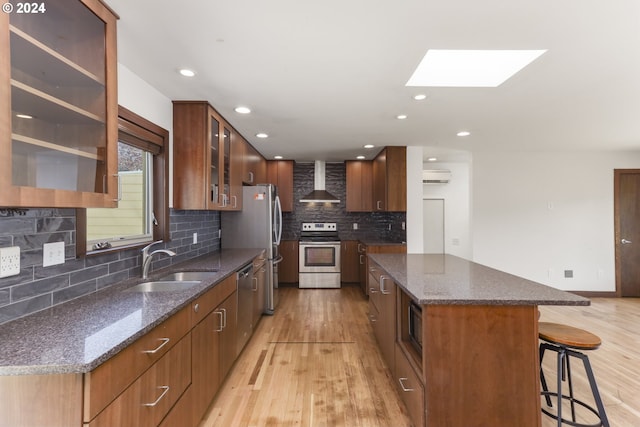 kitchen featuring a kitchen island, a breakfast bar, a skylight, stainless steel appliances, and wall chimney range hood