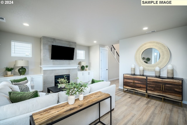 living room with light wood-style flooring, a fireplace, visible vents, and stairs