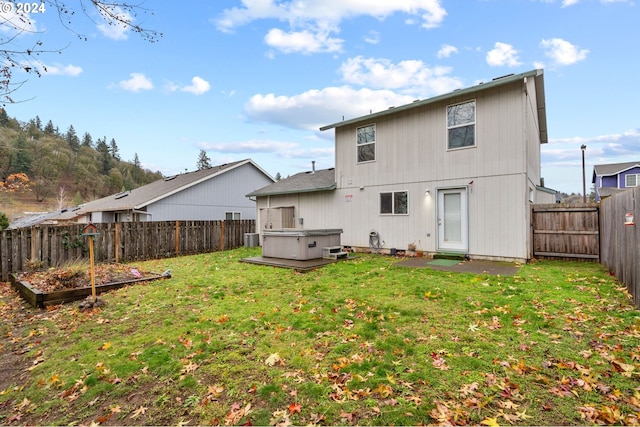 back of house featuring a yard and a hot tub