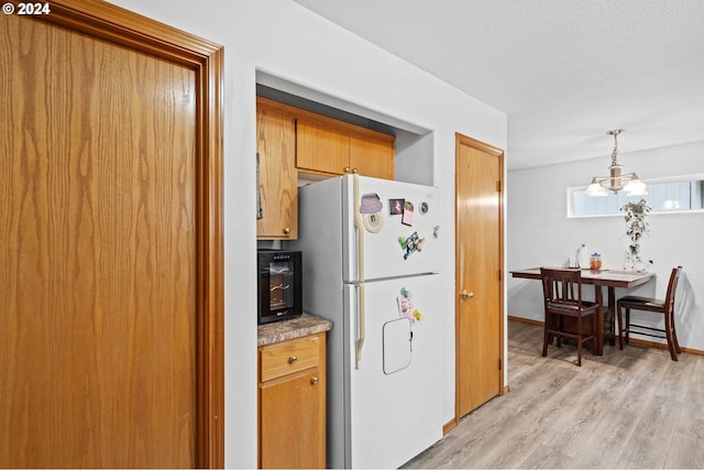 kitchen featuring a notable chandelier, white refrigerator, pendant lighting, a textured ceiling, and light hardwood / wood-style floors