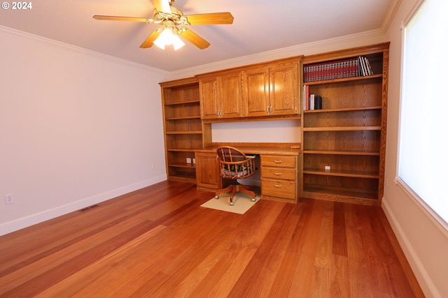 unfurnished office with crown molding, ceiling fan, built in desk, a wealth of natural light, and light hardwood / wood-style floors