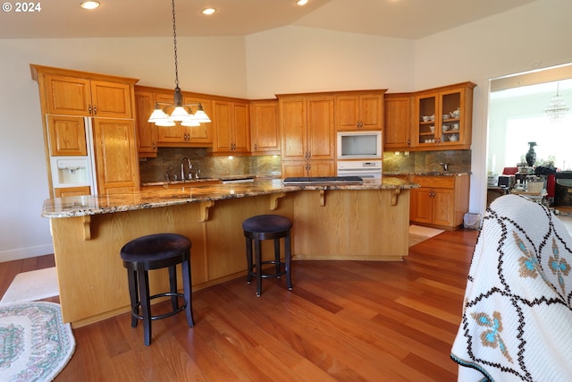 kitchen with white appliances, stone counters, sink, hanging light fixtures, and tasteful backsplash