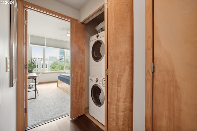 laundry room featuring dark wood finished floors, stacked washer and dryer, dark colored carpet, ceiling fan, and laundry area