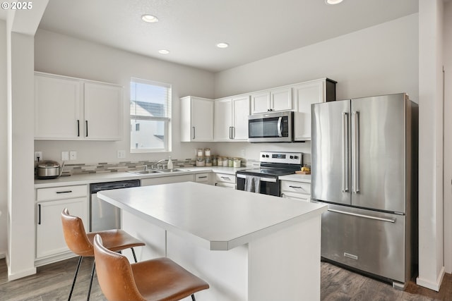 kitchen with a center island, a sink, stainless steel appliances, light countertops, and a kitchen bar